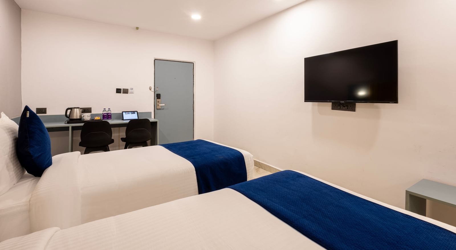 Side view of Superior Room featuring a bed with blue and white bedding, a yellow headboard, and modern furnishings including a desk and TV - Beestay Hotel Financial District, Hyderabad