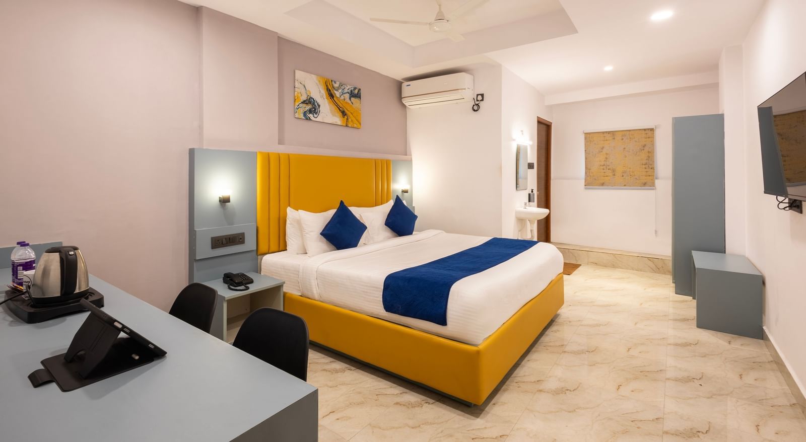 Full view of a modern Premium Room with a bed featuring blue accents, a work desk area, and a door on the left  - Beestay Hotels Financial District, Hyderabad 