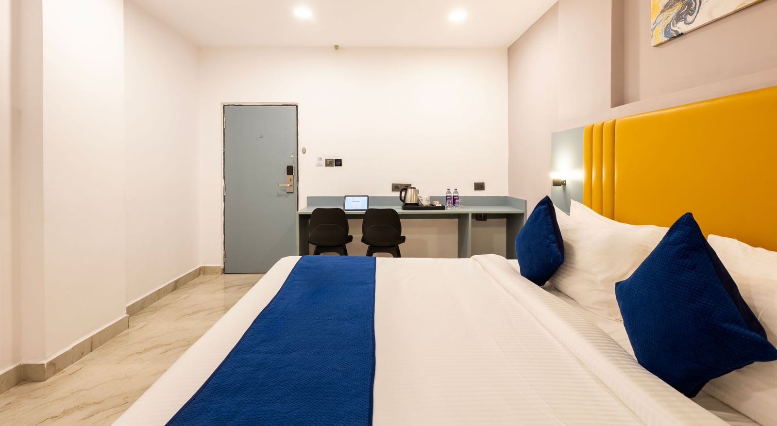 A modern Premium Room with a bed featuring blue accents, a work desk area, and a door on the left  - Beestay Hotels Financial District, Hyderabad 