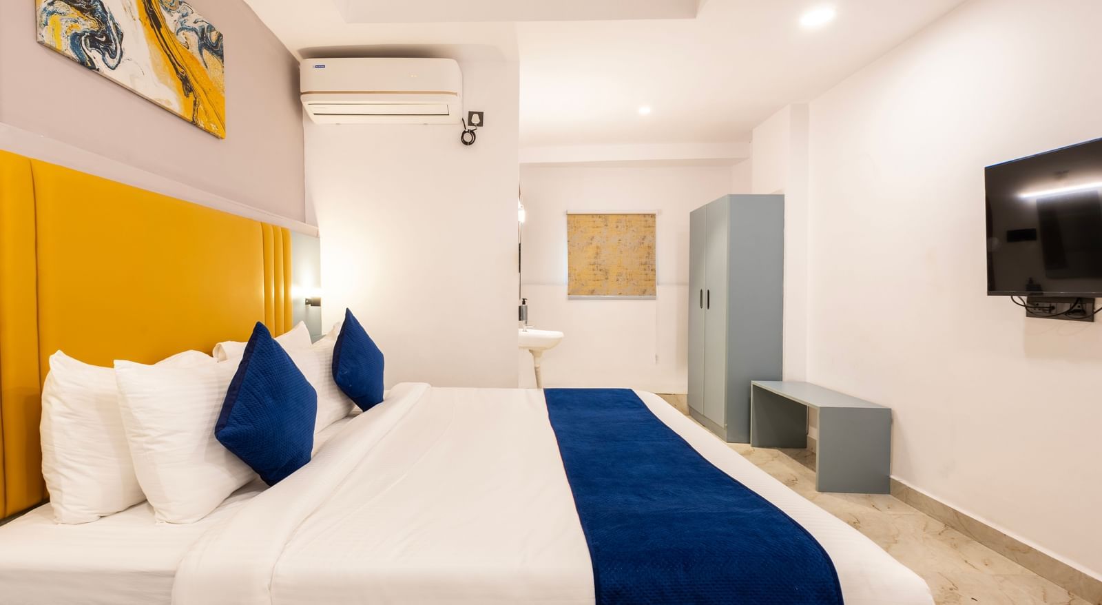 Side view of a modern Premium Room with a bed featuring blue accents, a work desk area, and a door on the left  - Beestay Hotels Financial District, Hyderabad 