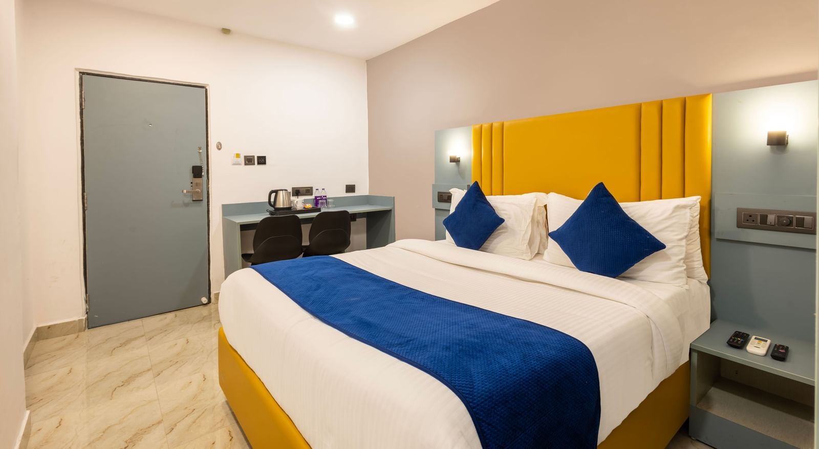 A Deluxe Room with a bed, blue and white bedding, a yellow headboard, and a desk area - Beestay Hotels Financial District, Hyderabad 