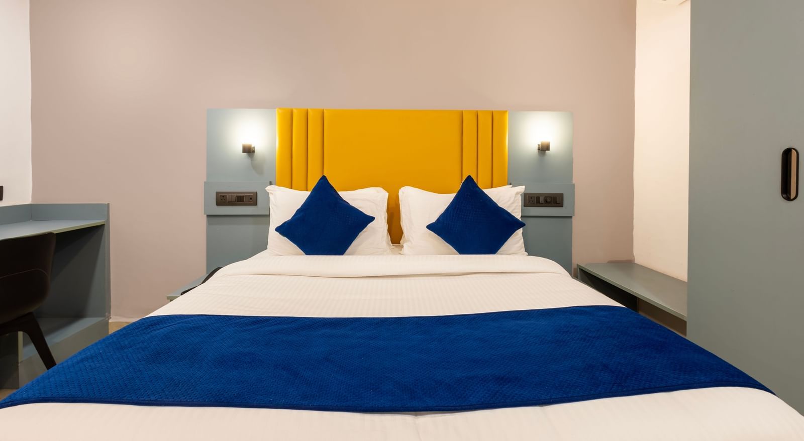 Close up of a Deluxe Room with a bed, blue and white bedding, a yellow headboard, and a desk area - Beestay Hotels Financial District, Hyderabad 