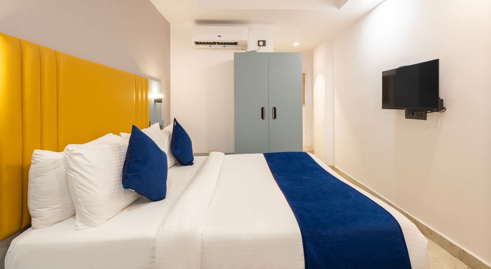 Side view of a Deluxe Room with a bed, blue and white bedding, a yellow headboard, and a desk area - Beestay Hotels Financial District, Hyderabad 