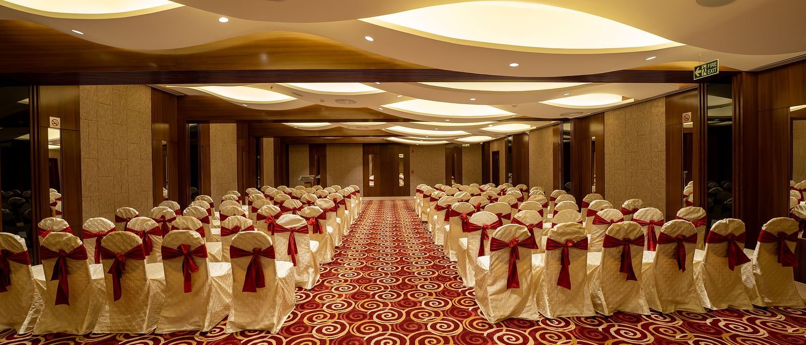 An image of a banquet hall set for an event with chairs draped in white covers and a red-and-white patterned carpet - The President Hotel, Kumara Park, Bangalore