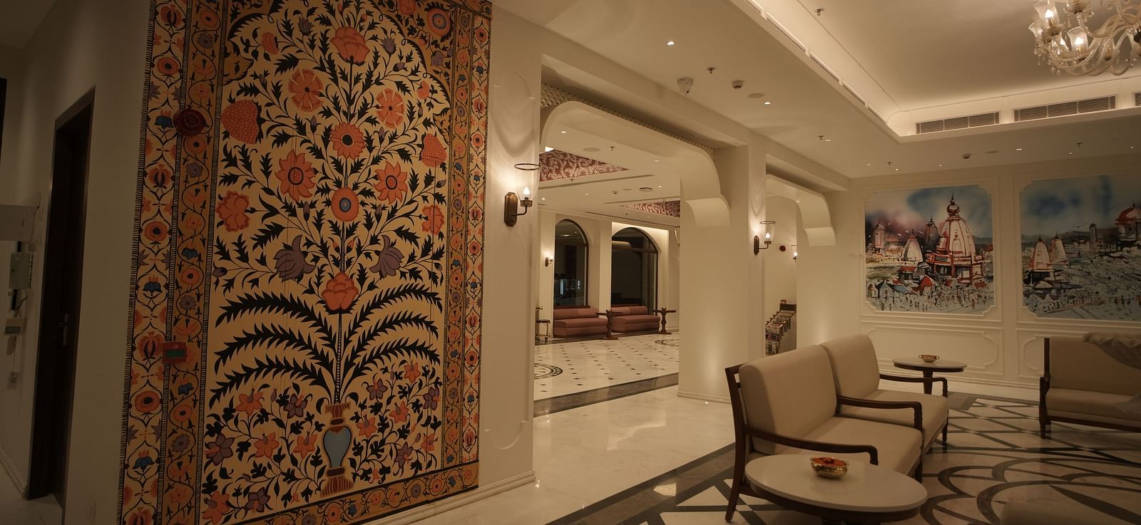 The reception area at Bhagirathi by RDB Atishay with warm lighting and intricate paintings on the walls.