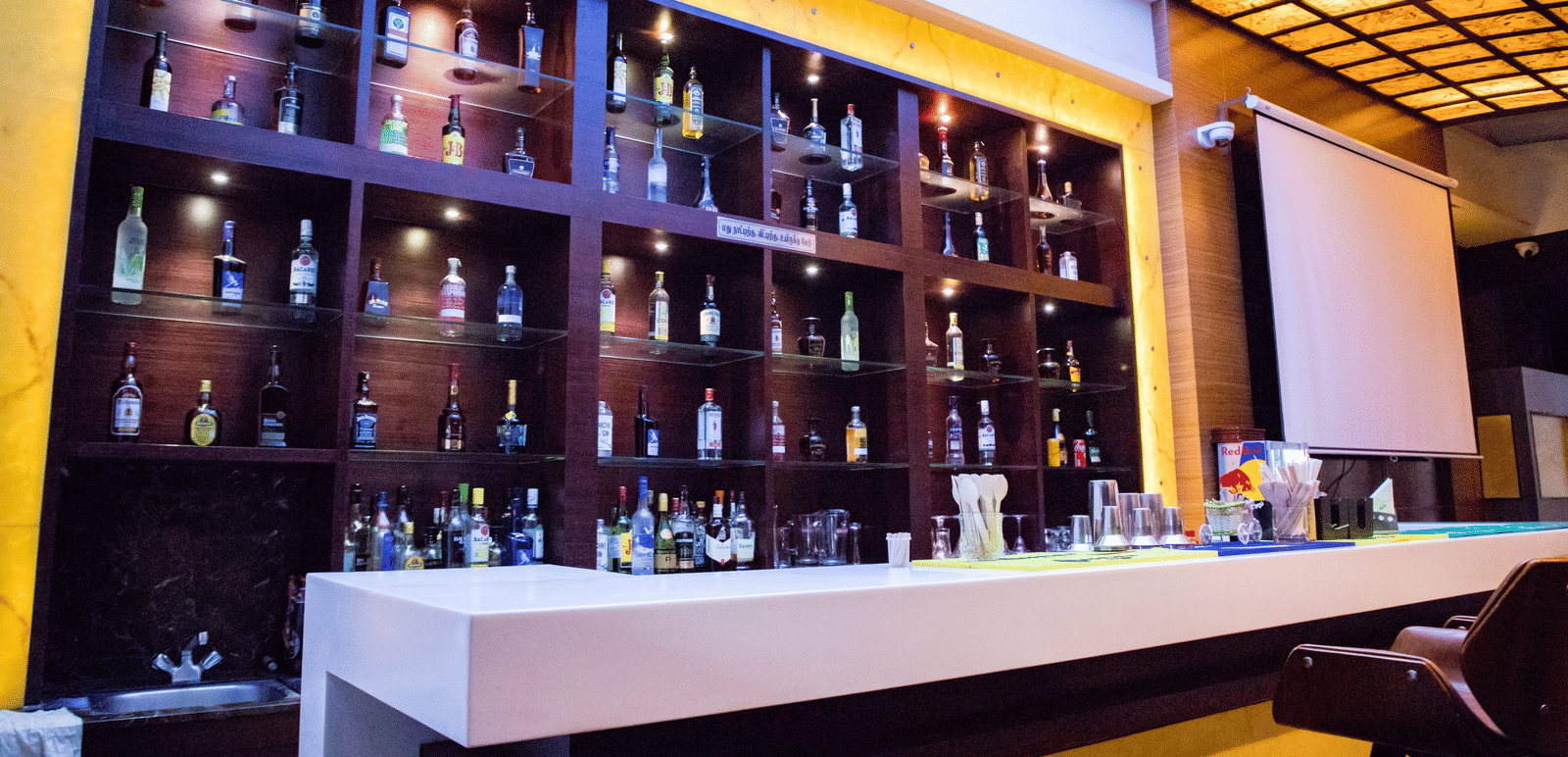 Side view of the bar featuring the bar counter and a display cabinet stacked with various liquor bottles on display at Benzz Park, Vellore.