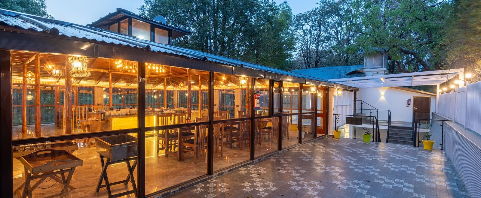 A shot of the restaurant taken from outside featuring the outdoor seating area and trees in the background - DLS The Emerald, Nainital