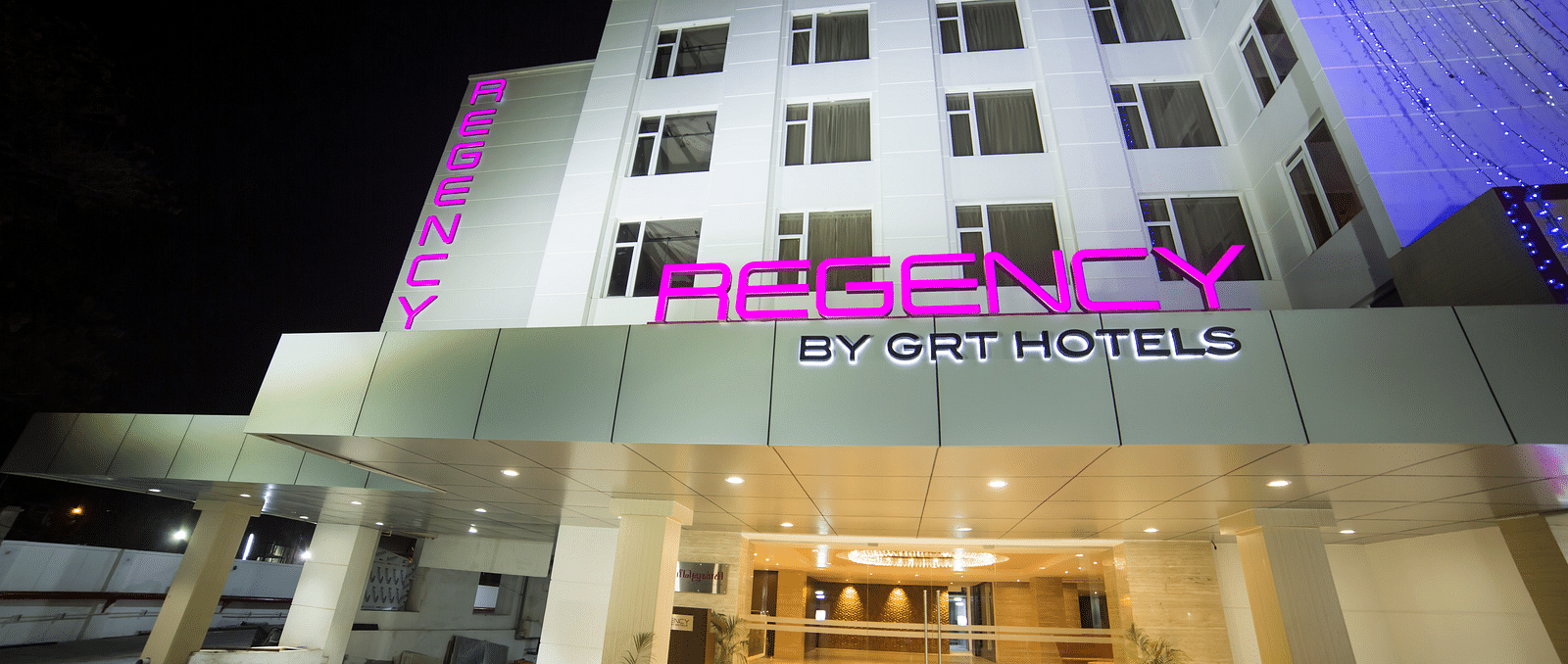 Regency GRT Hotels sign with purple letters and blue lights at night.