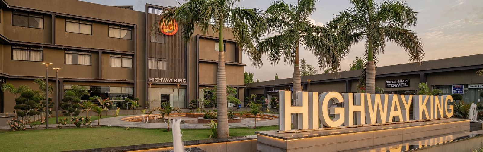 Exterior of Hotel Highway King, Behror, along with the well-manicured lawn and a signage with 'Highway King' written out on an elevated platform.