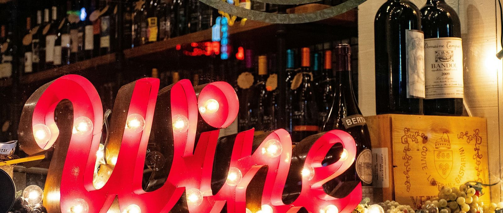 A vibrant wine bar setup with a glowing 'Wine' sign and bottles arranged for display.