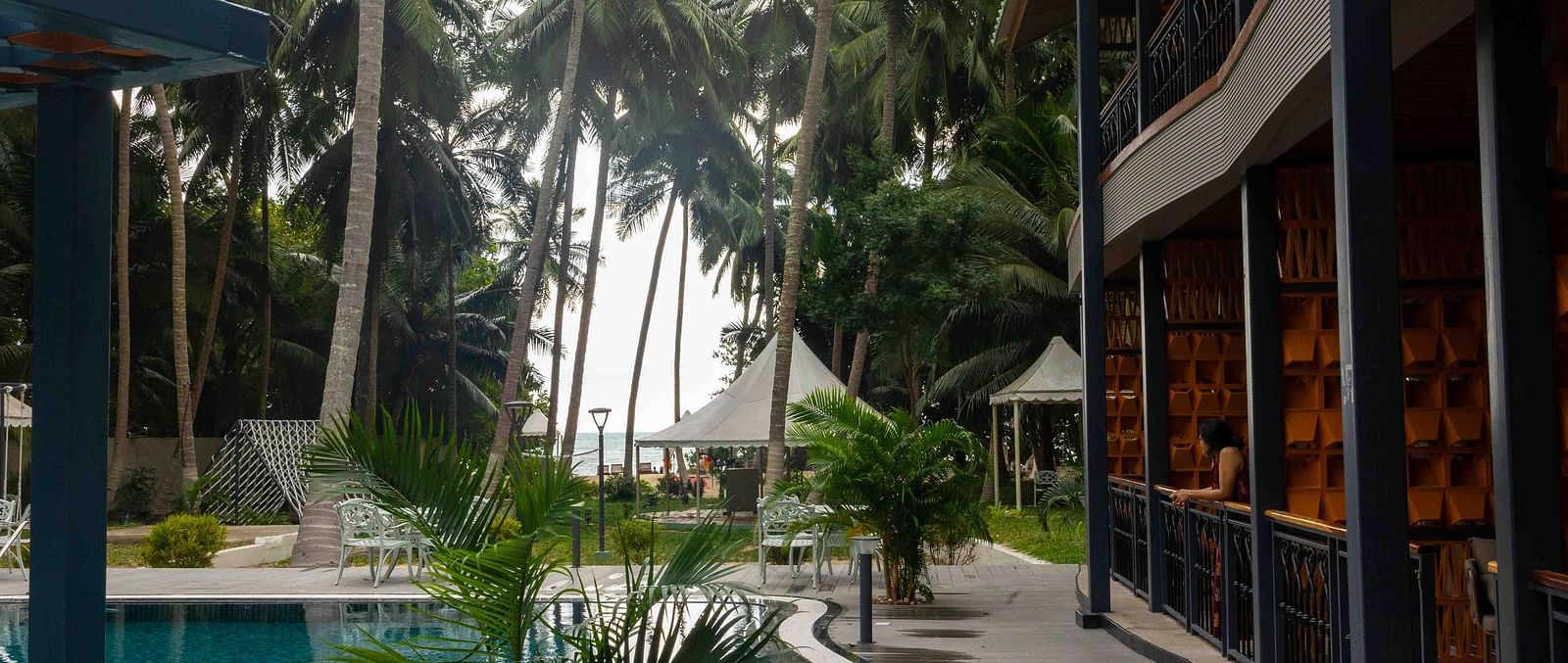 A view of a modern pool area with tropical palm trees surrounding the space. The architecture of the building is visible, providing a relaxing and elegant setting - Coral Reef Resort & Spa, Havelock