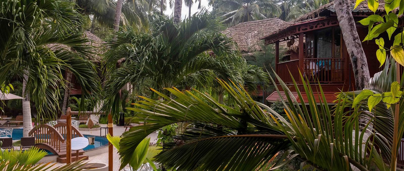 A view of a lush garden area at Coral Reef Resort and Spa in Havelock surrounding a pool, with palm trees and vibrant plants framing the space. The outdoor area is peaceful, creating a perfect environment for relaxation - Coral Reef Resort & Spa, Havelock