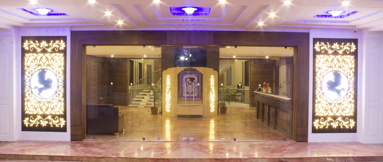 A brightly lit hotel lobby with intricate ceiling lights and columns | Daksh The Madhuvan Suites