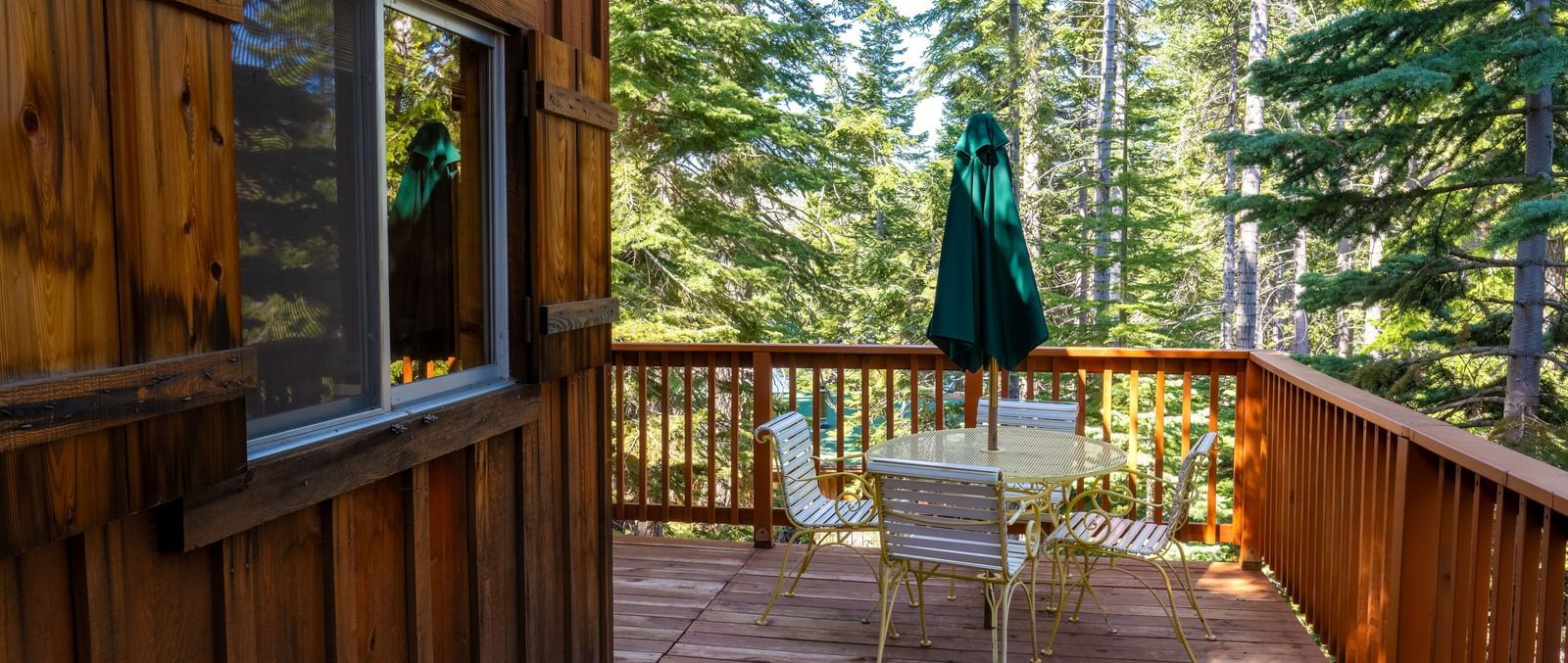 Wooden deck with table and chairs surrounded by tall pines outside a cabin at Kit Carson Lodge.