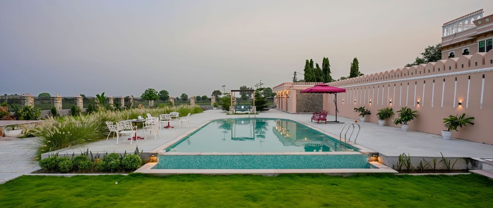 An eye-level shot of Mahendra Niwas, showcasing its luxurious swimming pool and well-maintained gardens under a soft, overcast sky.