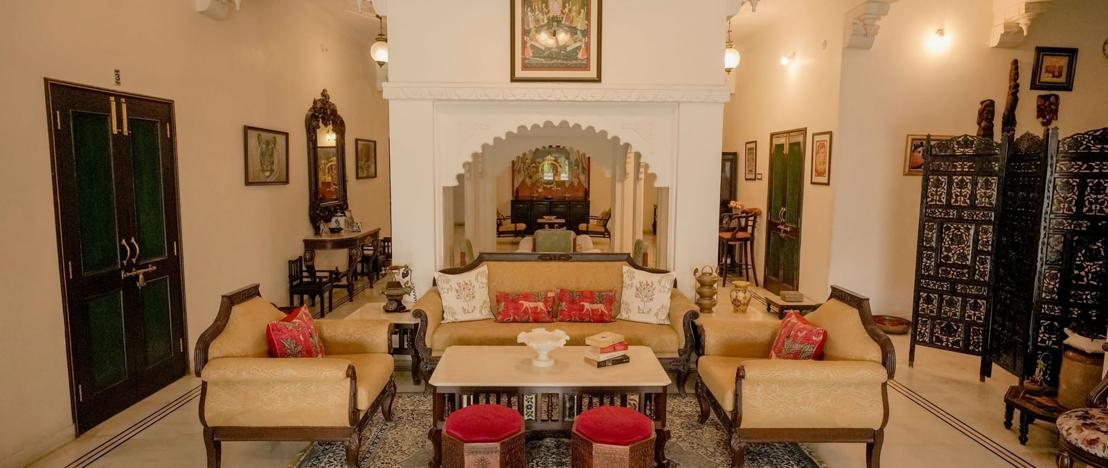  A cozy and elegant drawing-room in Mahendra Niwas, featuring twin-cushioned sofas, a central coffee table, and red ottomans.