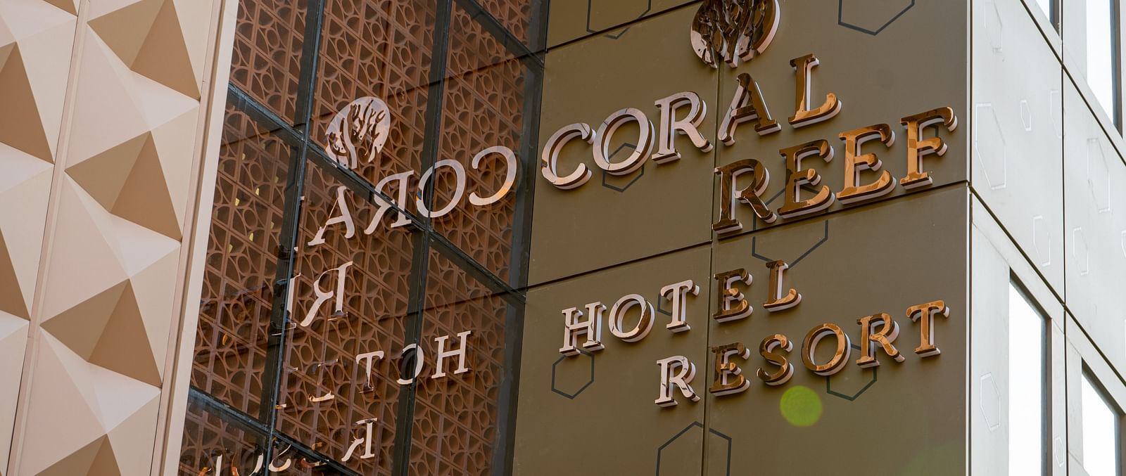 A wide view of the facade of a hotel at dusk, featuring geometric architectural patterns and vibrant signage - Coral Reef Hotel & Spa, Port Blair