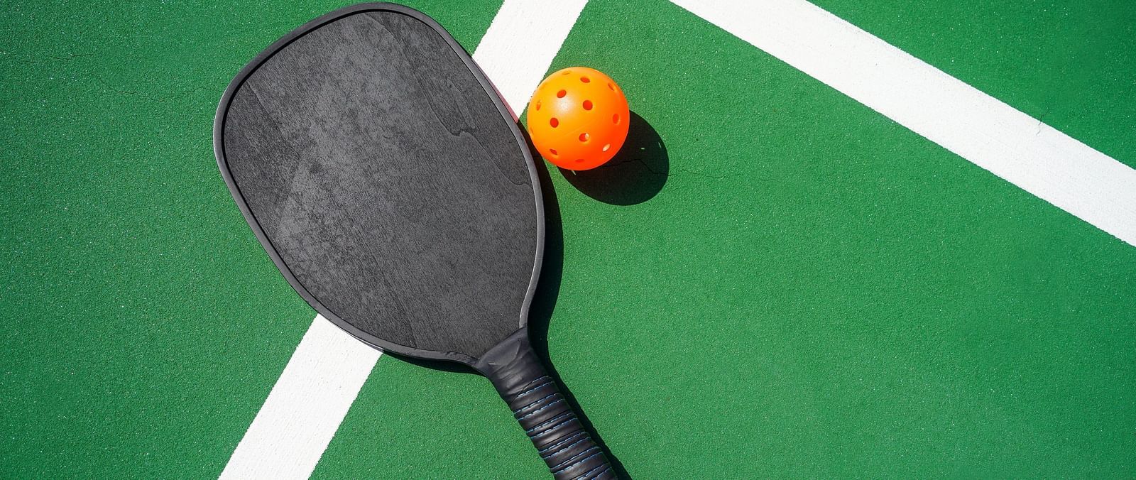 Image of a pickle ball and its racket kept on a green coloured court