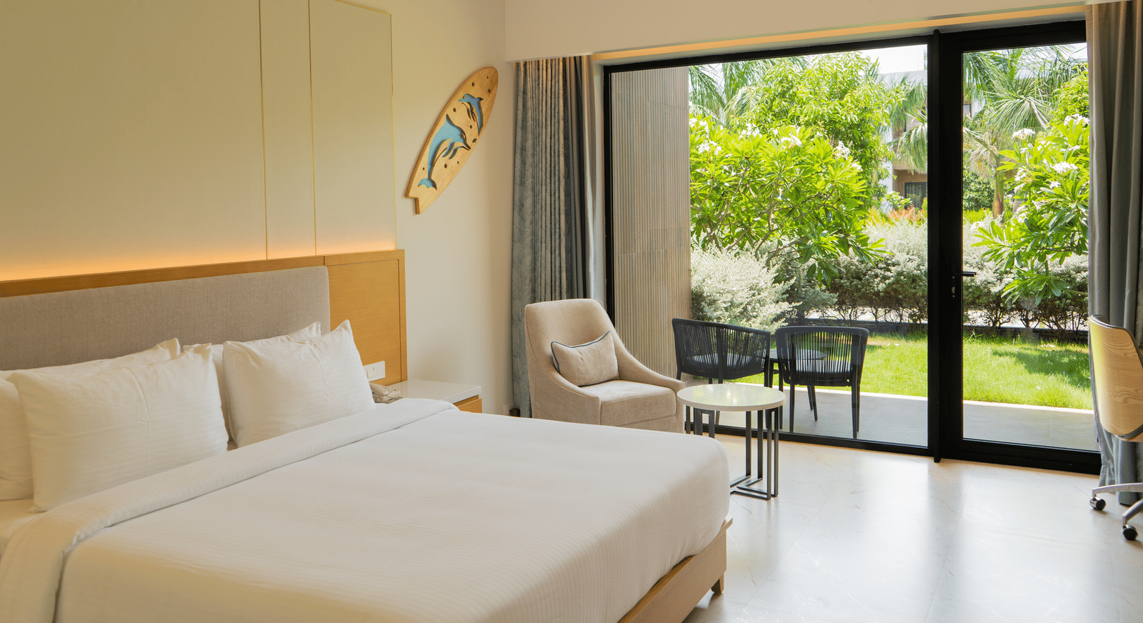 Garden Courtyard room at The Shore Trishvam, Pondicherry, with floor-to-ceiling glass doors opening to a lush tropical garden and outdoor seating.