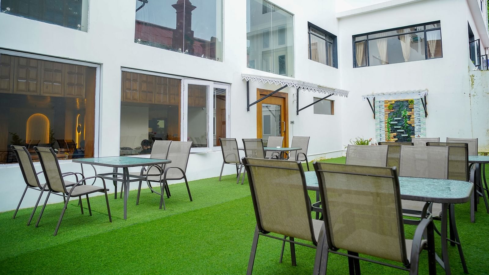 An outdoor dining area at Orsino Spa Resort with tables and chairs on green artificial turf, surrounded by white buildings.