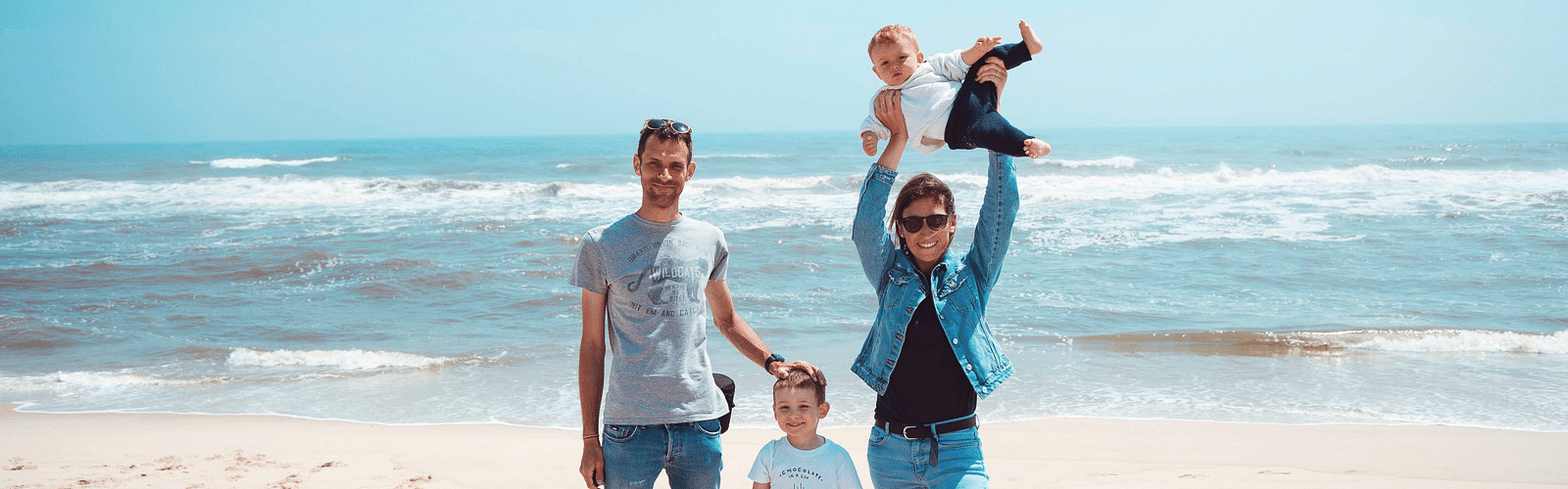 A family of four posing on the beach with white sands and blue sky in the background