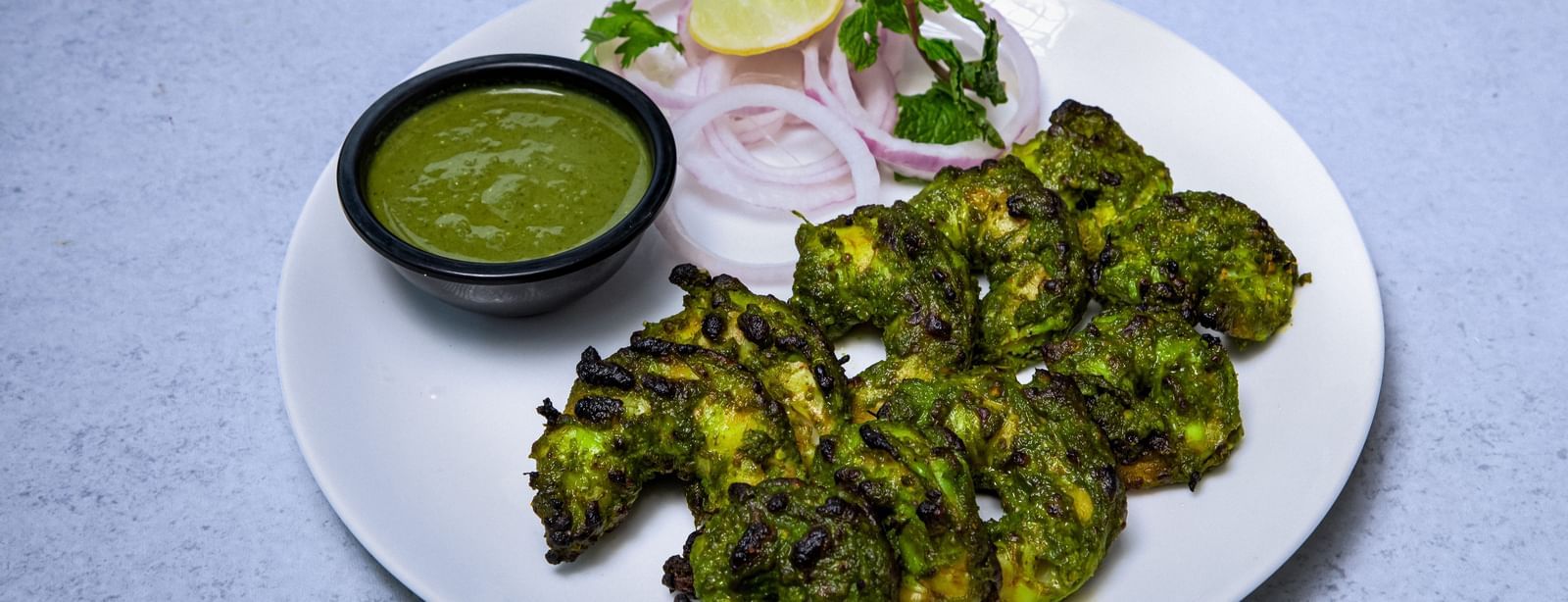 A plate of appetiser with a small bowl of green sauce and onion rings placed on side at The Hamuse Hotel, Kodaikanal.