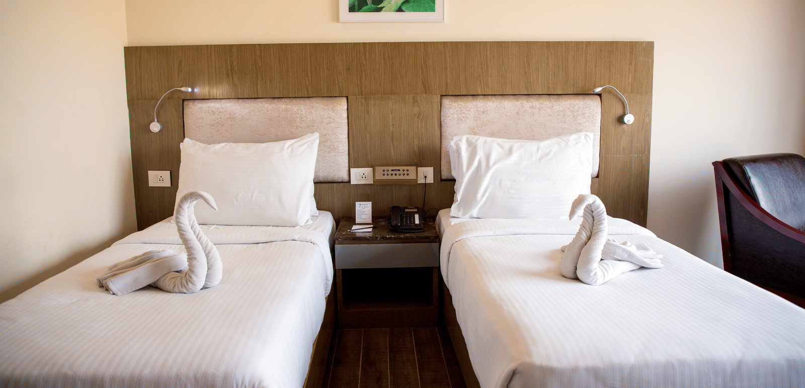 Close up shot featuring a twin beds in the Deluxe Room at Benzz Park, Vellore, with a bedside table between them.