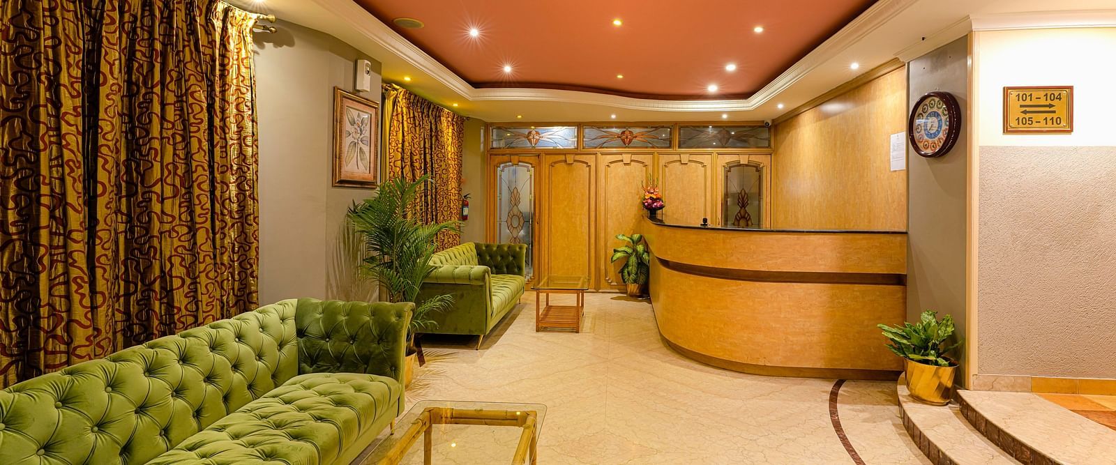 A cosy reception area with green couches and warm lighting - Cross Roads Inn, Bengaluru