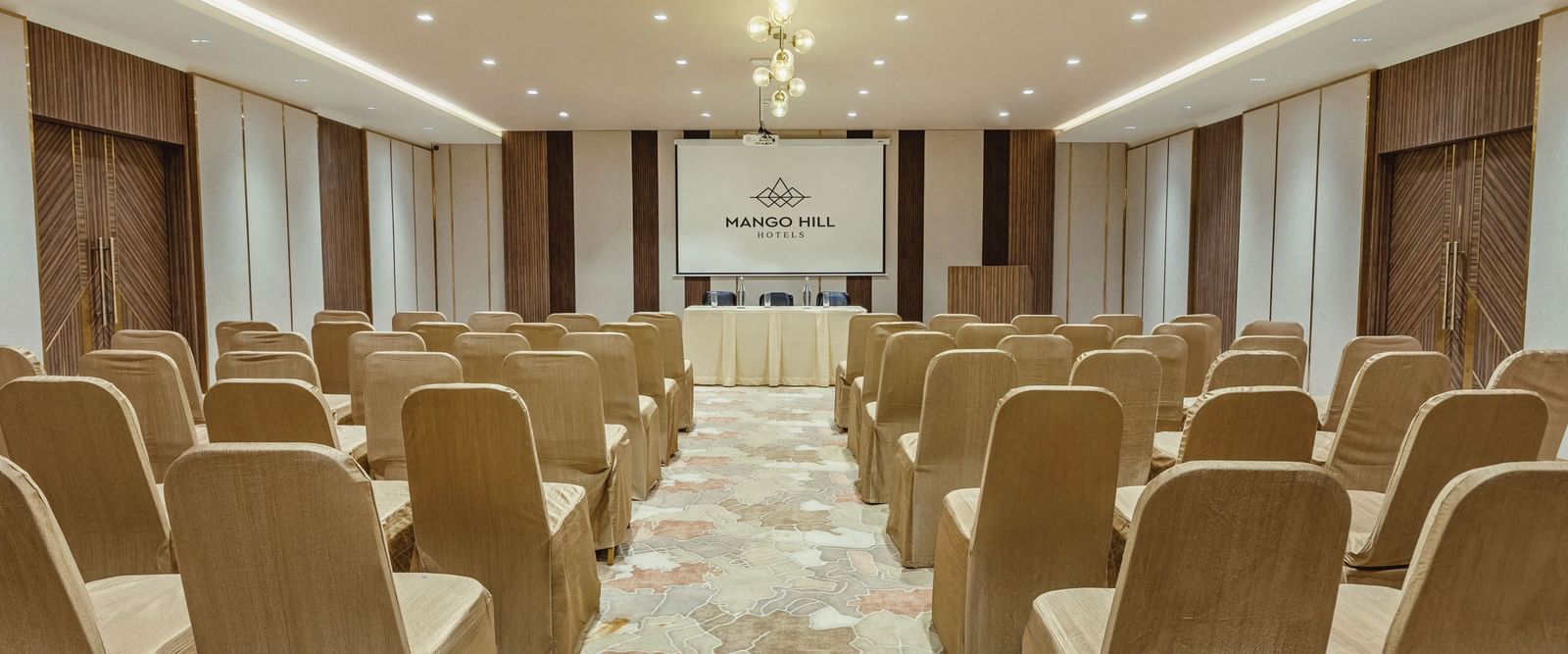 Banquet hall at Mango Hill Central, Chennai, with chairs arranged in rows facing a screen and a table at the front. The room is set up in a theatre style.
