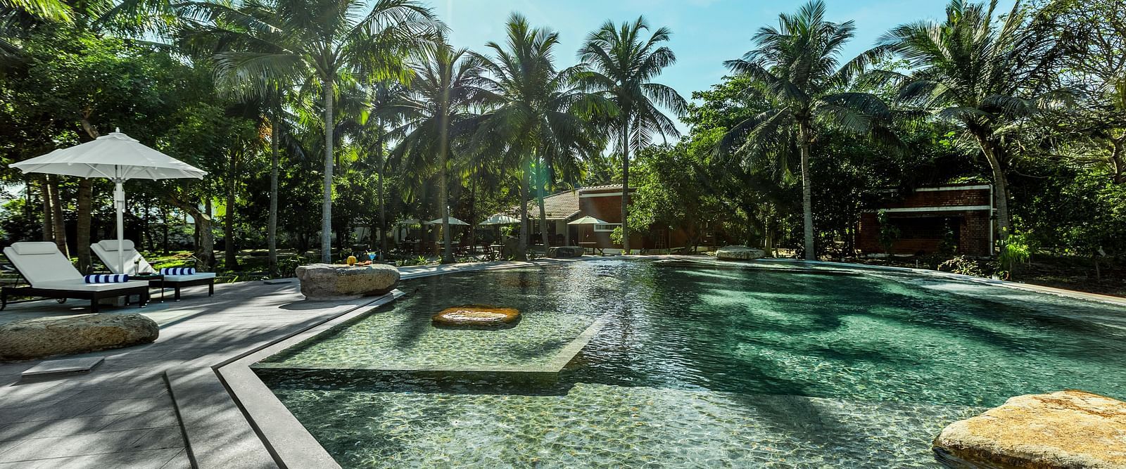 Resort swimming pool with lounge chairs and palm trees under a sunny sky | Mango Hill Shallow Beach Resort ECR