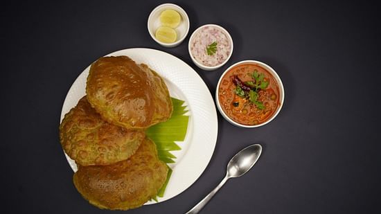 A plate of poori with channa, served with onions, lemon, and pickle.