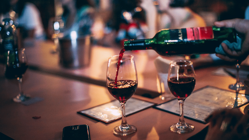 Red wine being poured into glasses at a lively bar or restaurant gathering