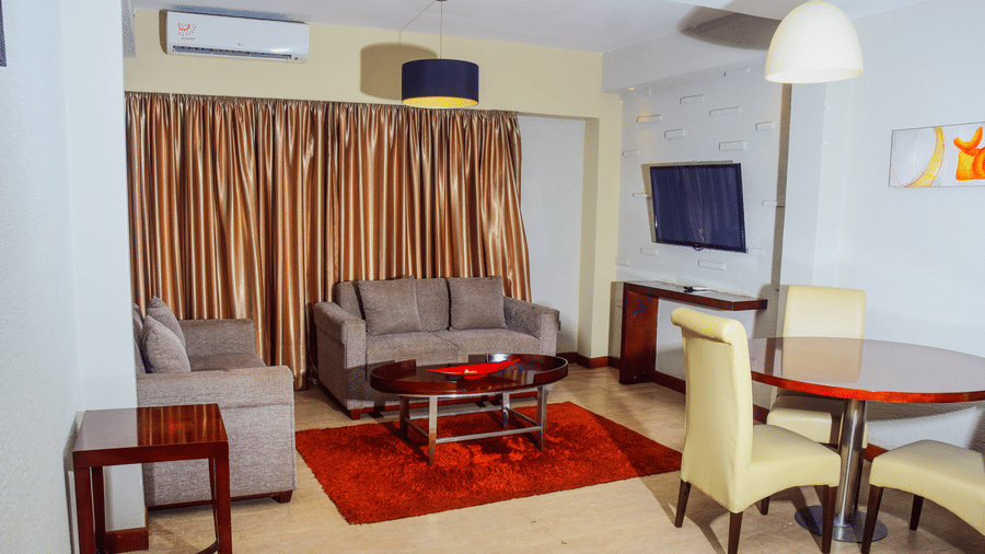 Spacious living area of a suite at The Zehneria, Nairobi featuring sofa seating, air-conditioning, a TV, and a dining table.
