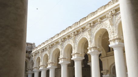 Elegant arcaded courtyard of Thirumalai Nayakkar Mahal featuring rows of towering white columns, intricate stucco work, and grand palace architecture.