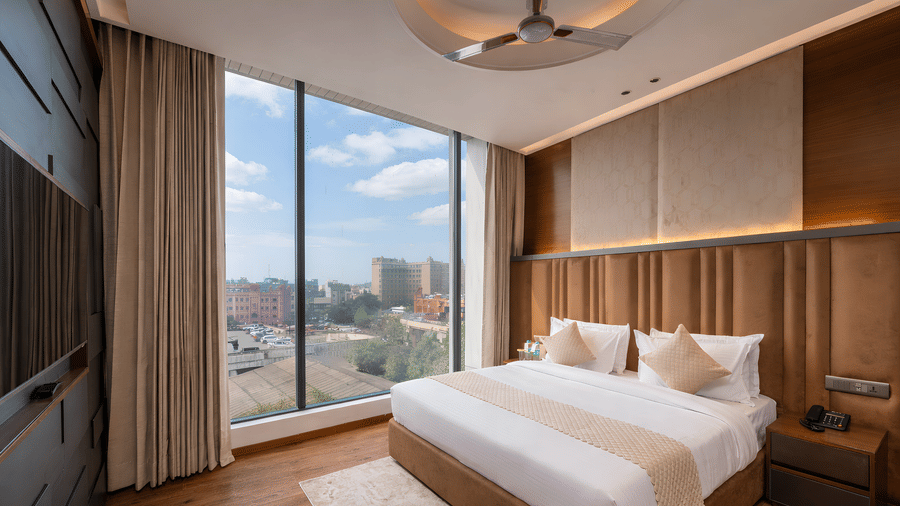   A bedroom with a king size bed, side tables, lamps, curtains, and a window showing buildings outside at DLS Hotels Amritsar.