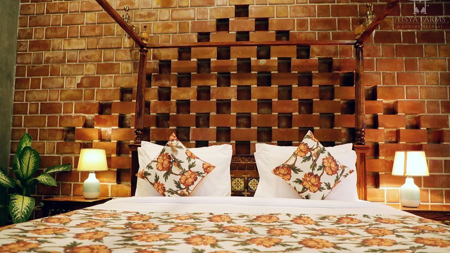 A bed with multiple pillows and an elegant, upholstered headboard at Tisya Farms, Gurgaon.