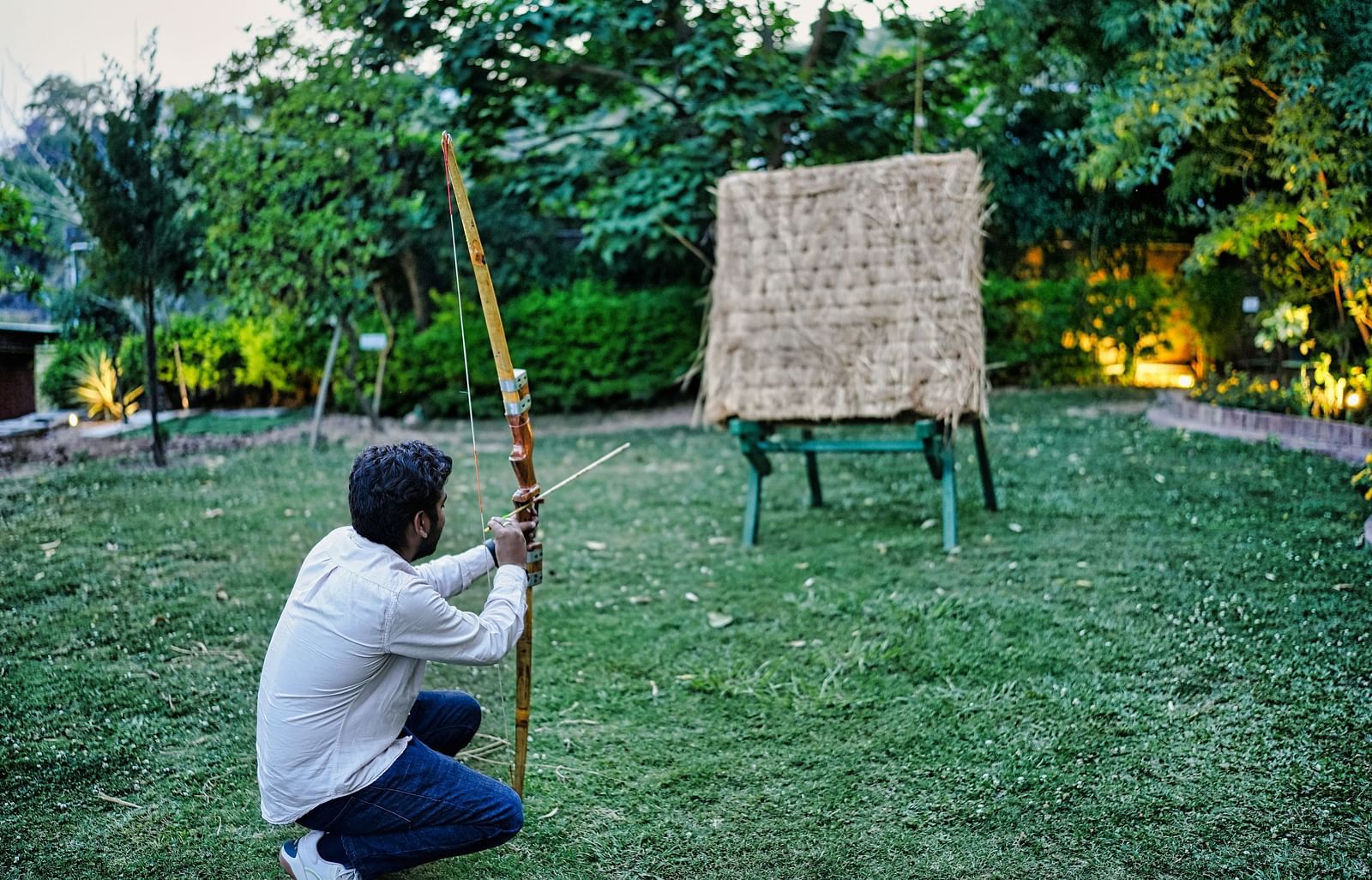 An image of a man trying out archery, aiming at the target, captured from back in a day light.