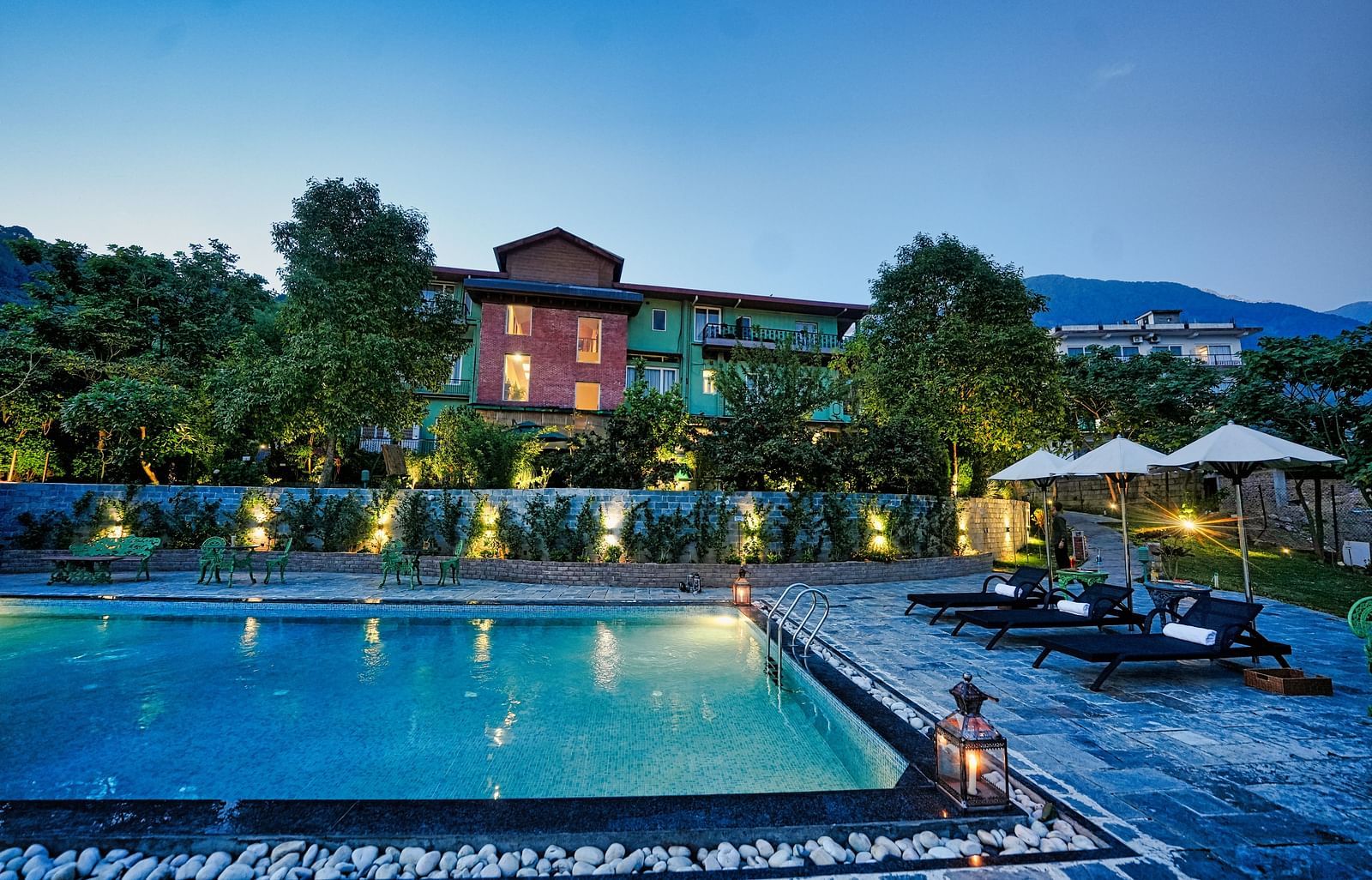 A picture with luxurious swimming pool, beautifully lit around and a scenic mountain view in the background - Atman, Dharamshala