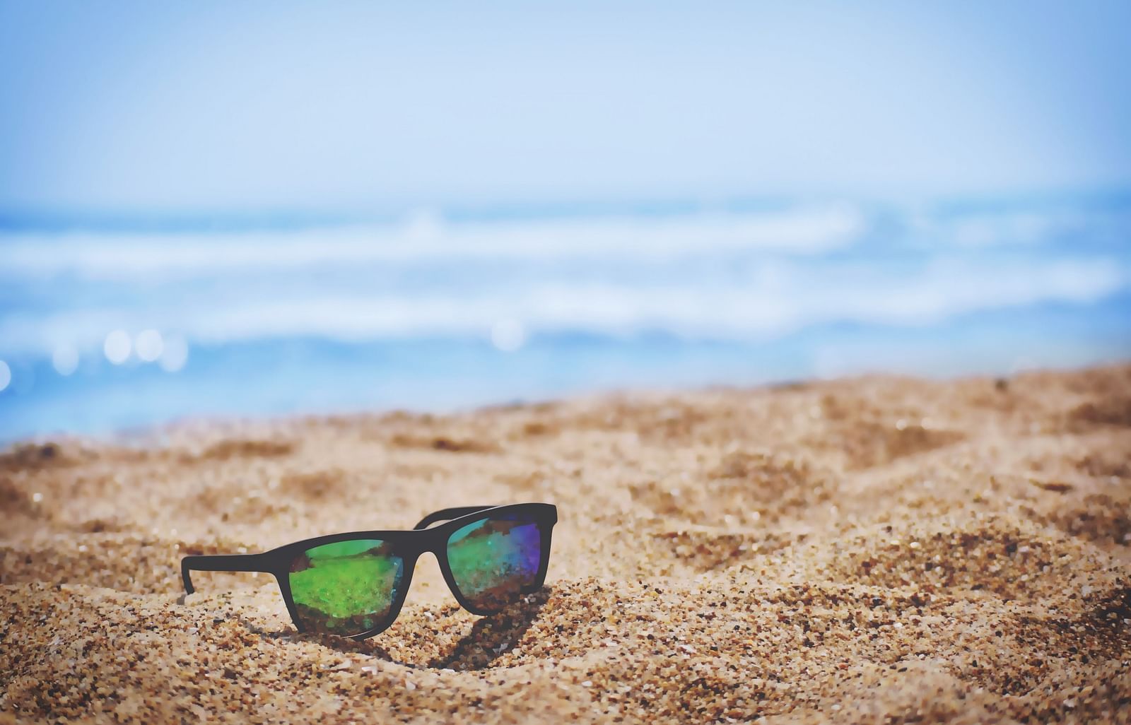Sunglasses resting on the sand by the beach.