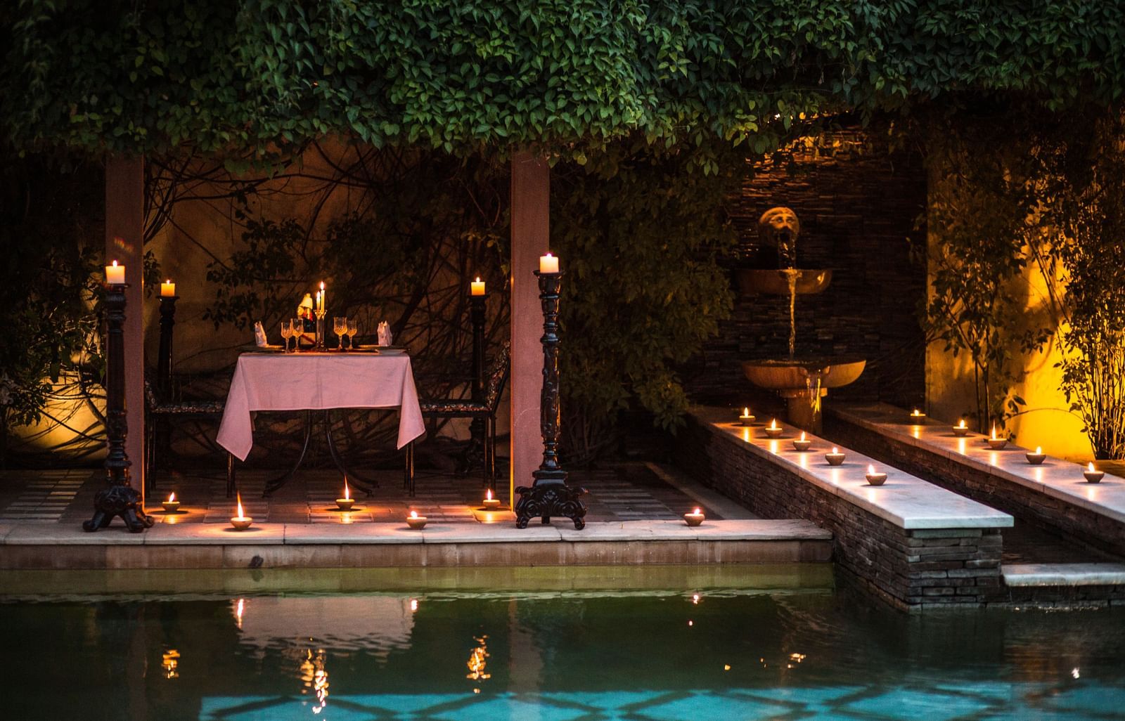 View of the outdoor setup with candles and a table next to water, similar to the first image, at Royal Heritage Haveli.