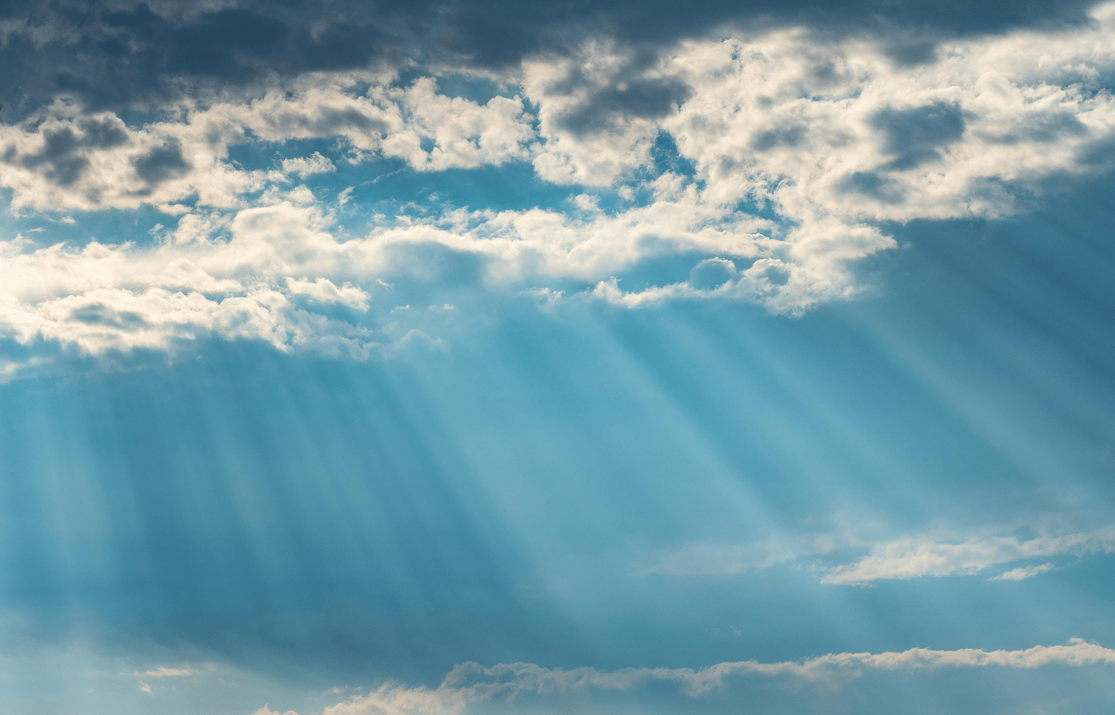 A close-up photo of sky with clouds and sunbeams breaking through.