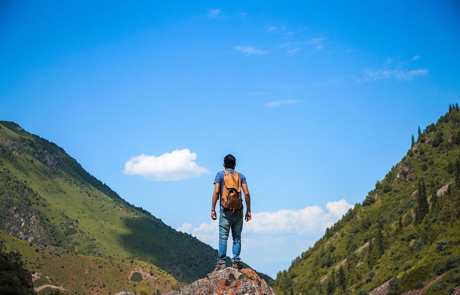 An image of a boy standing on a peak with a background of two hills and an open sky