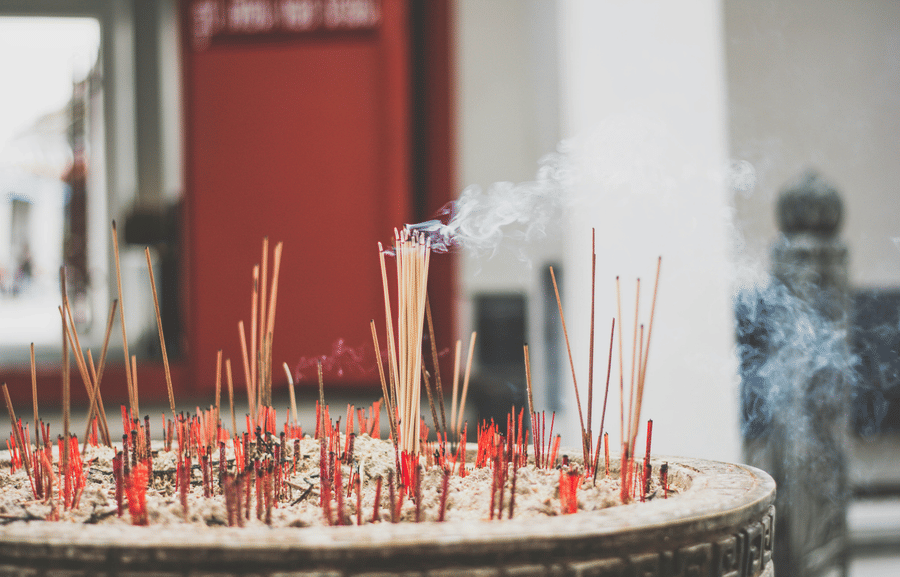A close-up view of numerous smoking incense sticks placed in a large, ancient-looking pot.