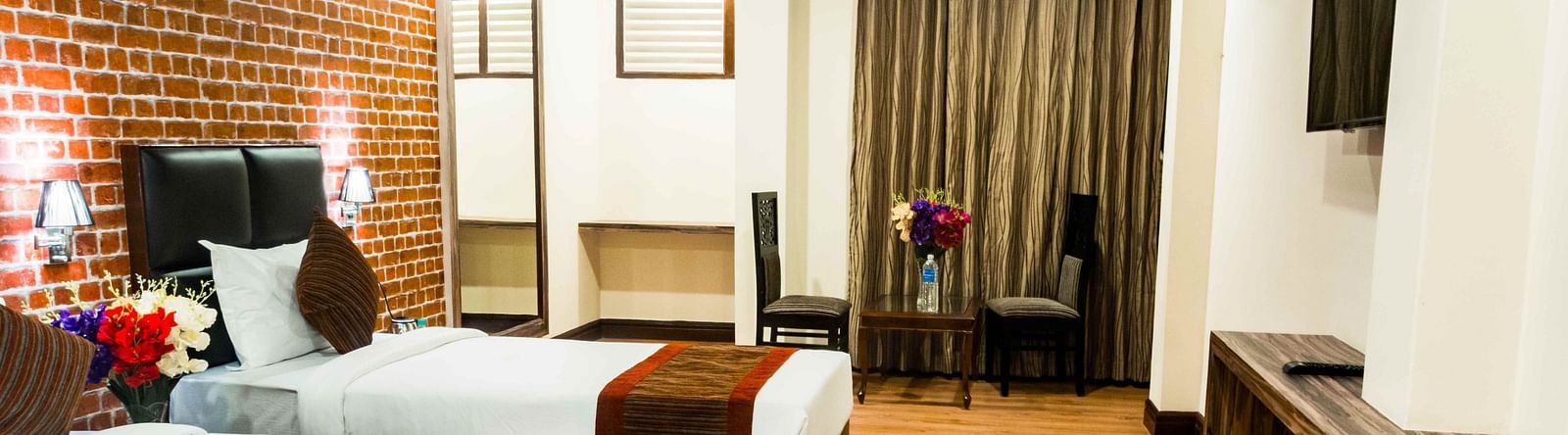 An image of the premium room with twin beds, bed side tables, flat screen TV, chairs and table, and floral decoration with bright lighting - Ecotel Tin Tin, Bijanbari