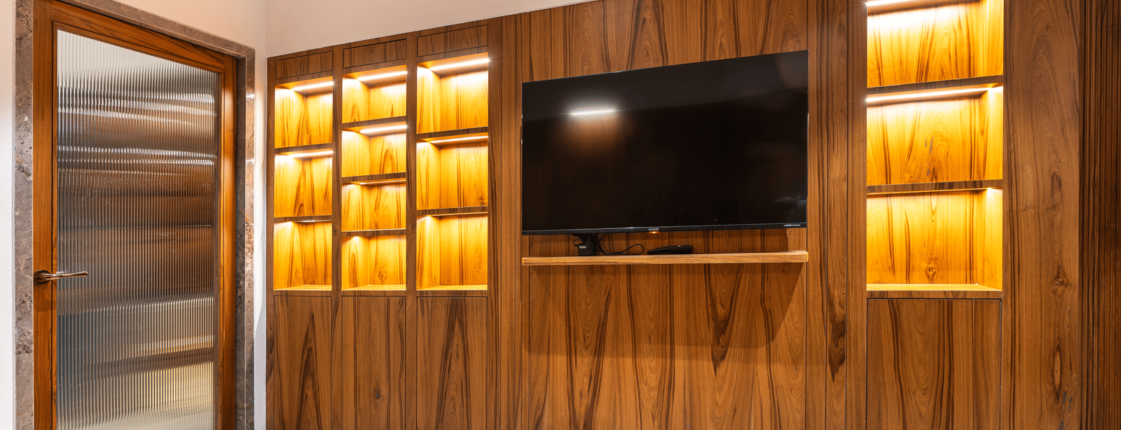 A room with wooden wall panelling, built-in television and illuminated shelves at Infiniti Hotel, Indore.