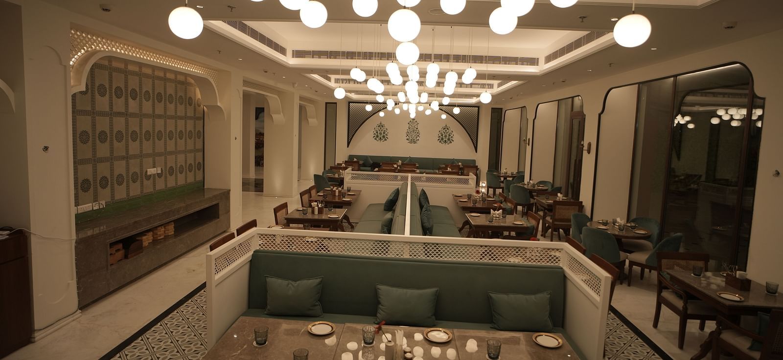 Full view shot of a restaurant with ample of warm lighting featuring well arranged dining tables along with cutlery Bhagirathi by RDB Atishay.