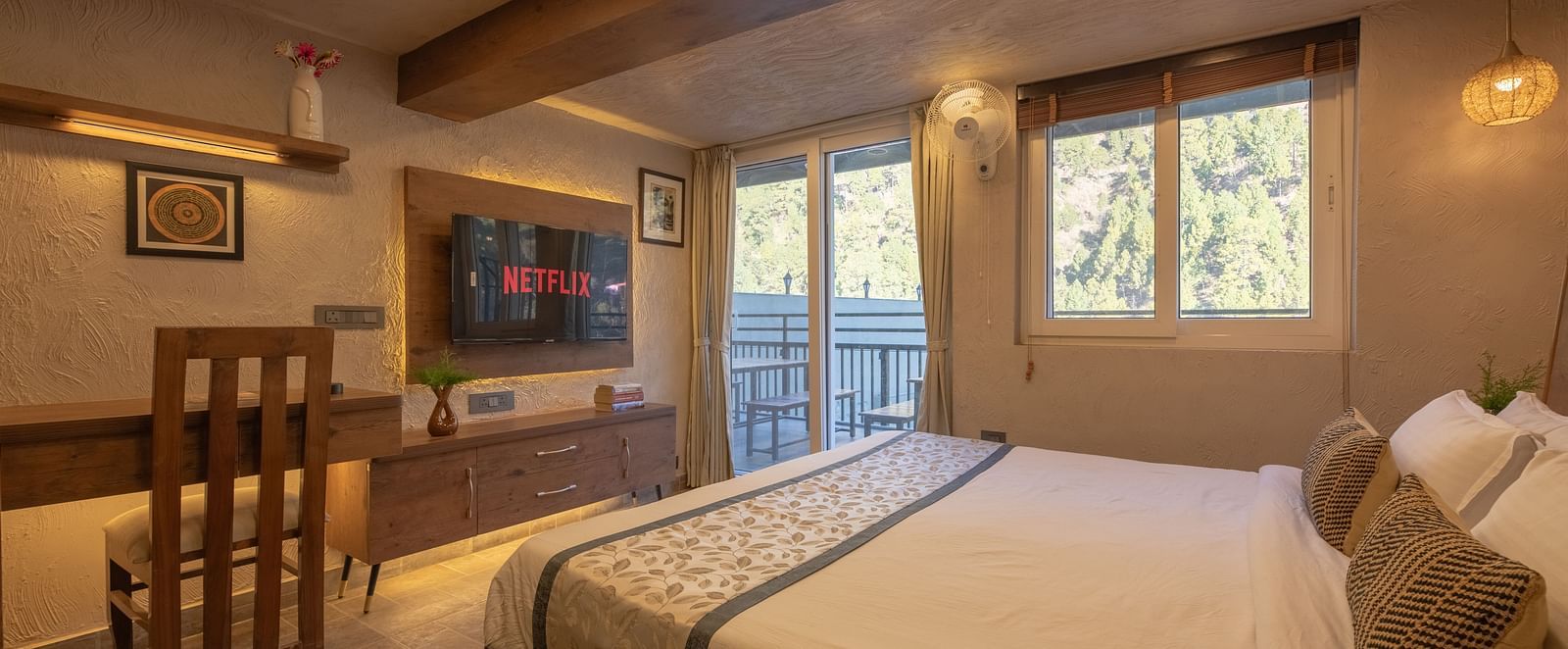 Room with double bed, TV, balcony doors, wooden beams on the ceiling, and soft lighting.