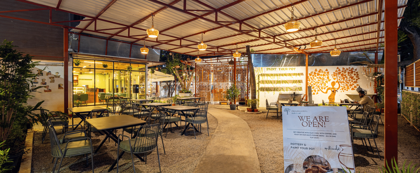 Claysutra Cafe & Restaurant at Kove Smart Stays seen during a darker time of the day, with ambient lighting, outdoor seating, and an overhead shed.