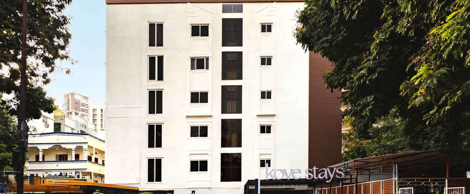 Facade of Kove Smart Stays seen on a bright day with a multi-storey structure, extended portico, and empty space in the front for parking.