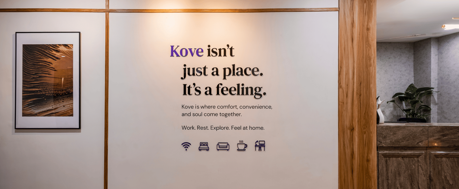 Lobby of Kove Smart Stays featuring a wall with the writing 'Kove isn't just a place. It's a feeling.' seen under a spotlight, beside the reception desk of the hotel.